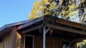 Una cabana de fusta amb un balcó, un porxo amb seients i una petita zona de jardí.