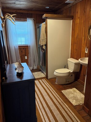 A wooden cabin bathroom with a toilet, sink, and a shower area. - Adorable 2 story lake front setting. (Georgetown)