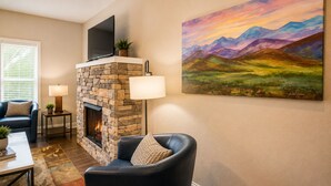 A living room with a stone fireplace, a flat-screen TV, a painting of mountains, and a blue armchair. - Golf View located in Valhalla Resort! Minutes to Oktoberfest! (Helen)