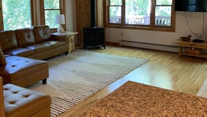 A spacious living room with a wooden ceiling, large windows, a fireplace, and a television.