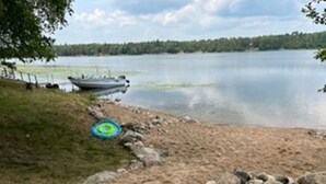 A lakeside view with a boat docked on the shore, a grassy area, and a stone pathway leading to the water.