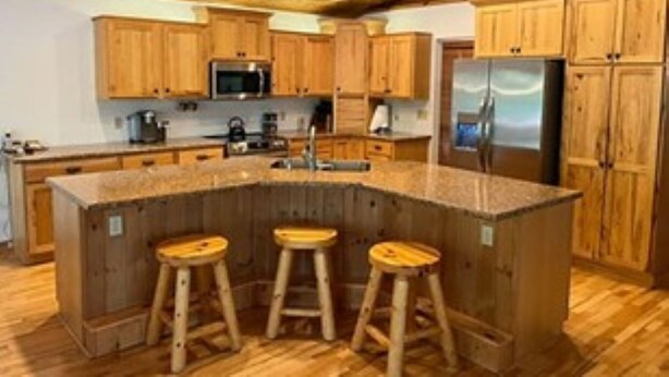 A kitchen with wooden cabinets, a central island with stools, and stainless steel appliances.