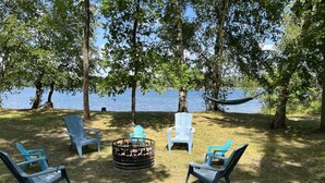 A lakeside seating area with Adirondack chairs and a fire pit.
