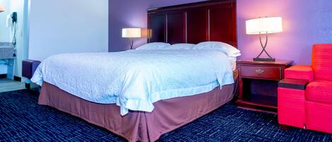 Una habitación de hotel con una cama grande, dos lámparas de noche, una silla roja y una mesita de noche de madera.