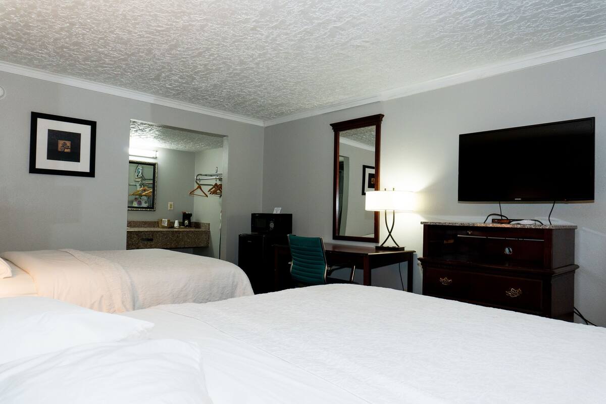 A hotel room with two beds, a desk, a TV, a mirror, and a dresser.