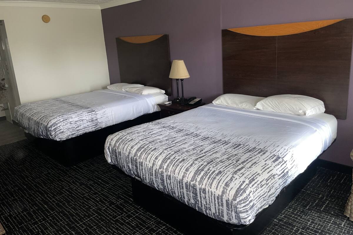 A hotel room with two beds, a nightstand with a lamp, and a headboard with a wooden accent.