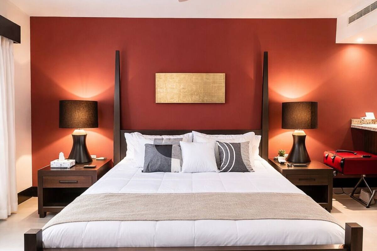 A modern hotel room with a large bed, two bedside tables, a ceiling fan, and a red accent wall.