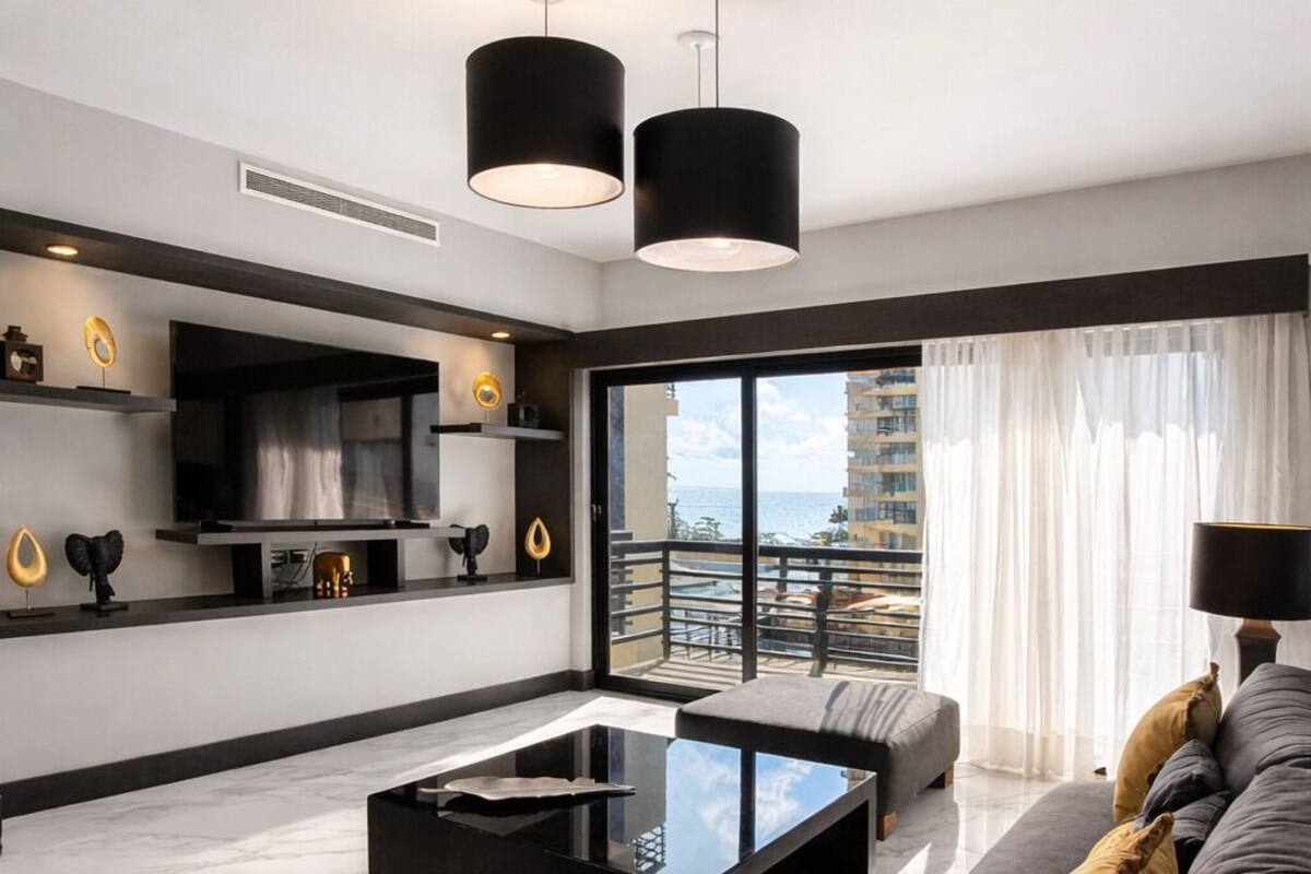 A modern living room with a black coffee table, grey sofa, and a balcony with a view.
