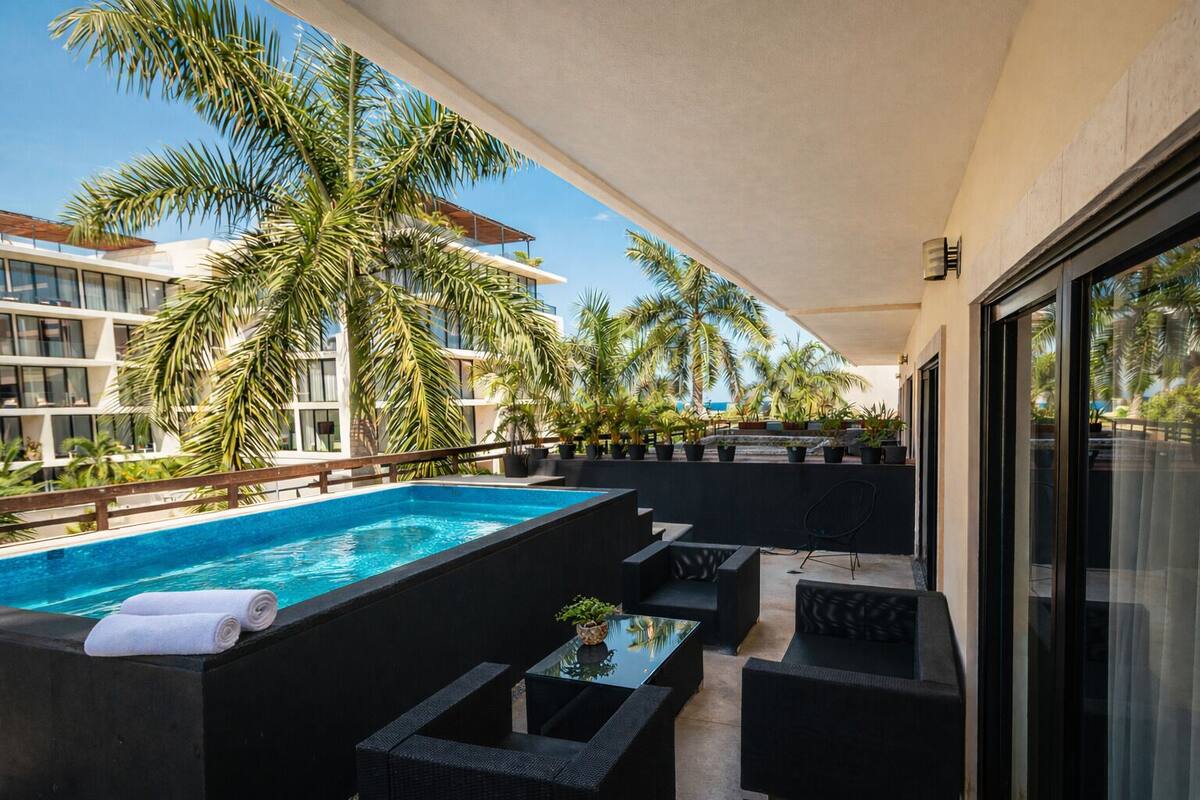 A rooftop pool area with a clear view of the surrounding buildings, palm trees, and a modern outdoor seating arrangement.