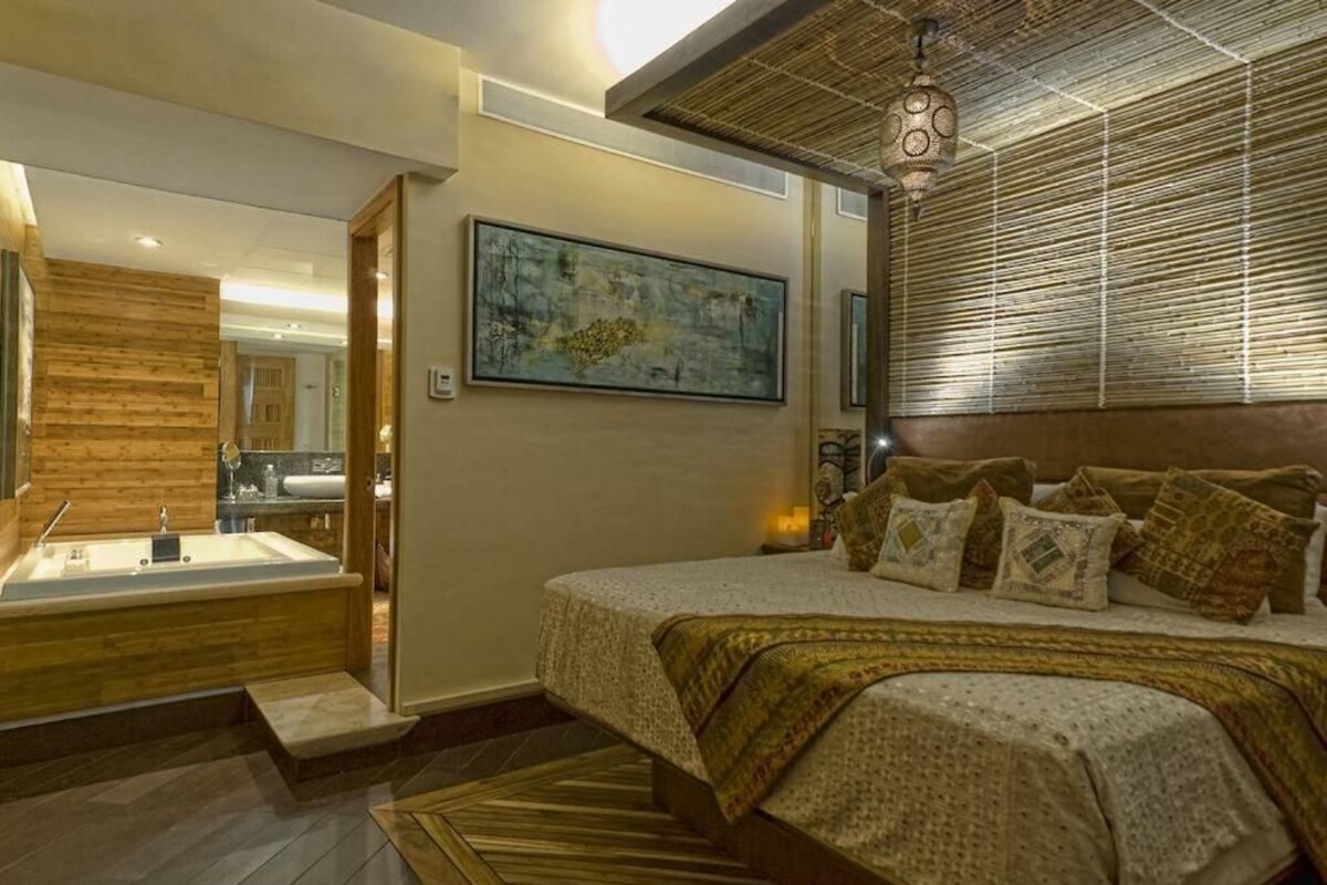 A modern bedroom with a large bed, a wooden panel wall, a painting, and a bathroom with a bathtub.