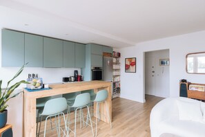 Cocina moderna con una isla central, taburetes de bar y un área de comedor con un sofá blanco.