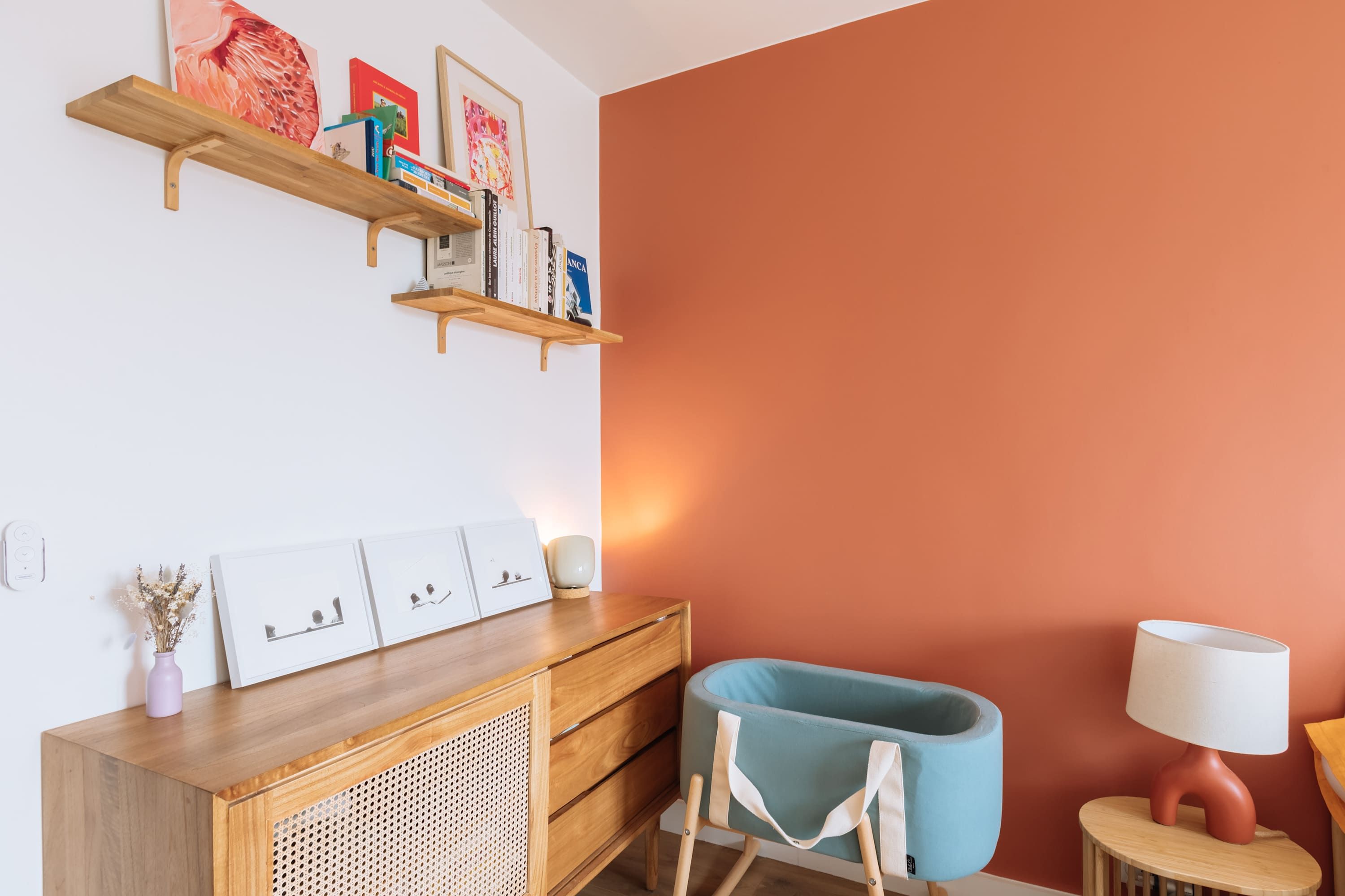 A room with a wooden console table, a blue chair, a small lamp, and a wall with a red accent.