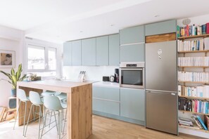 Una cocina moderna con armarios azul claro, un refrigerador de acero inoxidable, horno empotrado y cafetera. Hay taburetes de bar y una isla de madera con pileta.