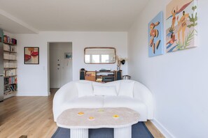 A living room with a white sofa, a coffee table with citrus designs, a bookshelf, and a mirror.