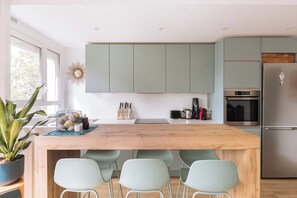 A modern kitchen with light green cabinets, a wooden island with bar stools, and stainless steel appliances.