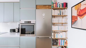 Una cocina moderna con armarios azul claro, un refrigerador de acero inoxidable, un horno empotrado y un estante de madera con libros.
