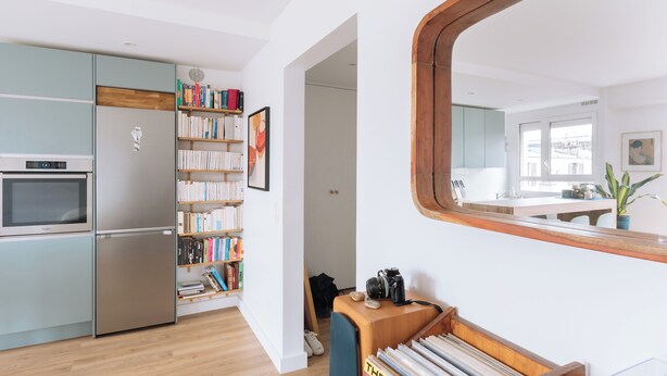 Una cocina moderna con horno y refrigerador integrados, una estantería llena de libros y un aparador de madera con una cámara.