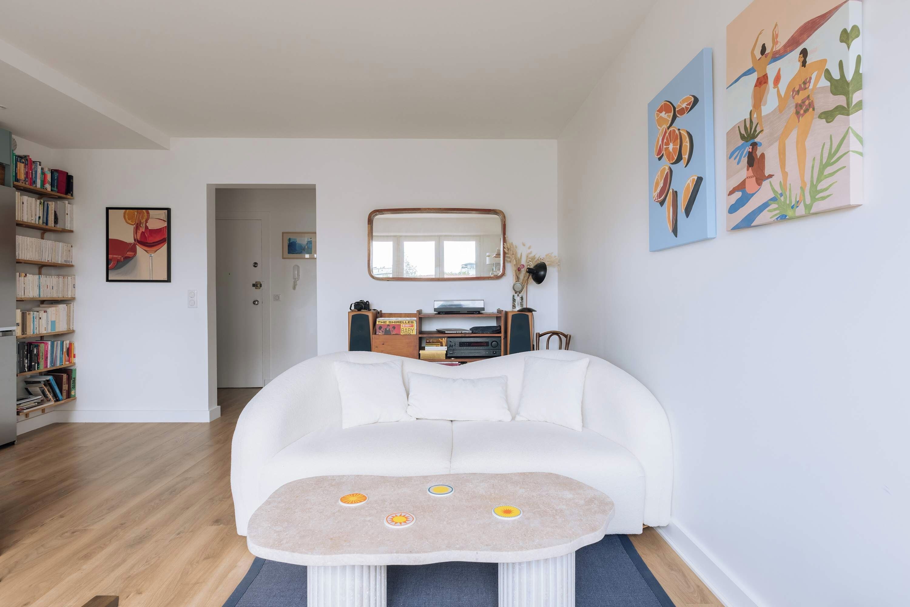 Uma sala de estar moderna com um sofá branco, uma mesinha redonda e uma estante repleta de livros.