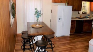 A kitchen with wooden cabinets, a white refrigerator, and a dining area with a wooden table and four stools. - Waterfront 5 Bedroom (Karnack)