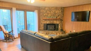A living room with a stone fireplace, a large sectional sofa, a rocking chair, and a flat-screen TV mounted on the wall. - Waterfront 5 Bedroom (Karnack)