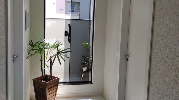 A hallway with a potted plant, a doormat, and a view of a building outside. - Bueno's Hotel Francisco Beltrão (Francisco Beltrao)