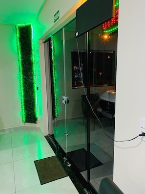 A modern hotel lobby with a green vertical light installation, a glass door entrance, and a dining area visible through the glass. - Bueno's Hotel Francisco Beltrão (Francisco Beltrao)