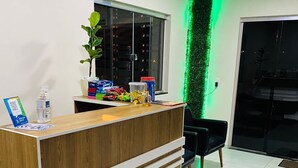 A reception desk with a wooden finish, a potted plant, and a green decorative wall. - Bueno's Hotel Francisco Beltrão (Francisco Beltrao)