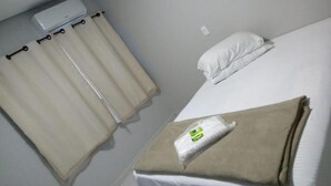 A hotel room with a bed, a white pillow, a beige blanket, and a white curtain. - Bueno's Hotel Francisco Beltrão (Francisco Beltrao)