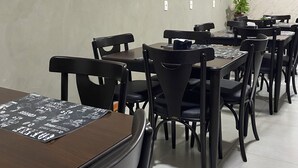 A dining area with multiple tables and chairs, a potted plant, and a marble wall with framed pictures. - Bueno's Hotel Francisco Beltrão (Francisco Beltrao)