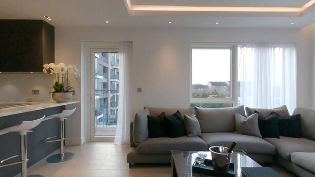 A modern living room with a grey sofa, a coffee table, and a bar area with stools. - Chelsea Harbour 2-bed Apartment in London (London)