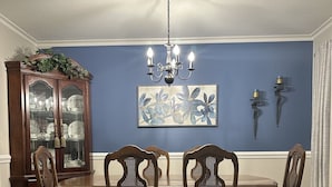 A dining room with a wooden table and chairs, a chandelier, a cabinet, and a painting on the wall.