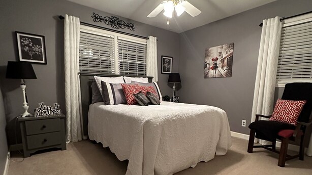 A bedroom with a bed, a nightstand, a chair, a ceiling fan, and two windows with curtains. - Walking Bear Retreat near North Greenville University in a quiet country retreat (Landrum)
