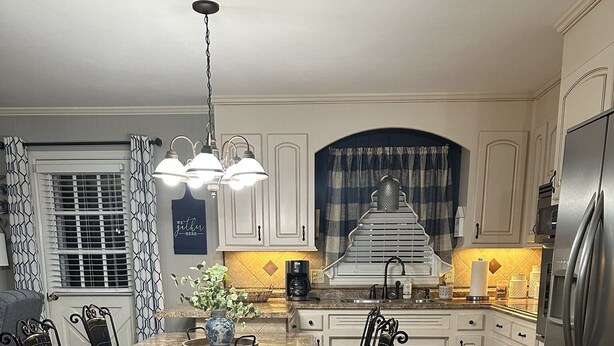 A modern kitchen with white cabinetry, a central island with chairs, a stainless steel refrigerator, and a pendant light above the island.