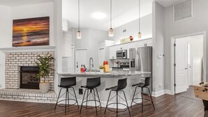 Una cocina moderna con una isla central, muebles blancos, electrodomésticos de acero inoxidable y una chimenea de ladrillo.