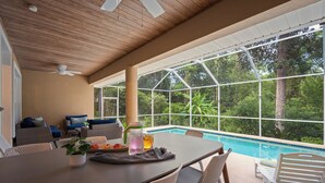 Un área junto a la piscina con una mesa, sillas y un sofá.
