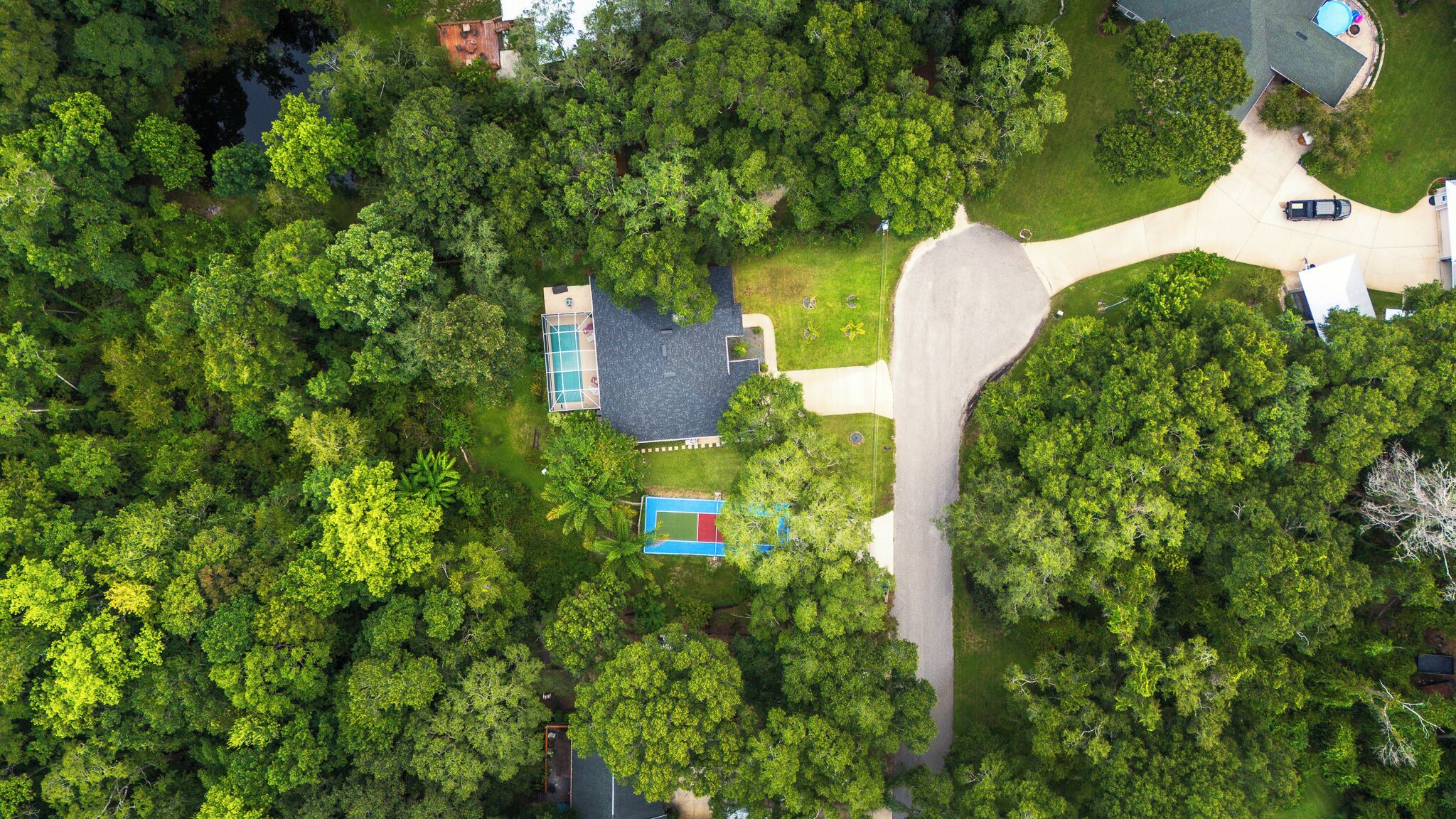 An aerial view of a residential area with a swimming pool, tennis court, and a road.