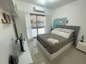 A modern bedroom with a large bed, a bedside table, a TV, and a window with curtains.