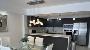 Une cuisine moderne dotée d’un îlot central, d’appareils électroménagers en acier inoxydable et de luminaires suspendus.