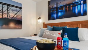 A hotel room with a bed, a bowl of popcorn, two bottles of soda, and a tray.