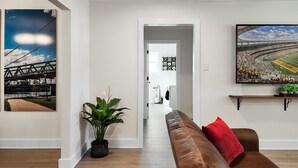 A living room with a brown leather couch, a red pillow, a potted plant, and two framed pictures on the walls.