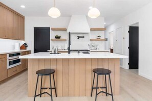 A modern kitchen with wooden cabinets, a white island with two stools, and pendant lighting. - Stylish 4bd/3bath - Spanish Home, central in LA (Los Angeles)