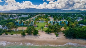An aerial view of a coastal resort with beachfront villas, palm trees, and a mountain backdrop. - BEST AQUATIKA PENTHOUSE: truly beachfront, 10 beds, 5 rooms, 10 person capacity. (Vieques)