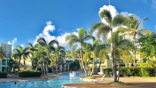 A swimming pool surrounded by palm trees and a building with a poolside area. - BEST AQUATIKA PENTHOUSE: truly beachfront, 10 beds, 5 rooms, 10 person capacity. (Vieques)