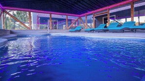 An indoor swimming pool with blue water, surrounded by lounge chairs and a covered area with wooden beams and neon lighting. -  7 bedrooms, 4 bathrooms, located in Beach Lake, PA. Sleeps 16, Max capacity  21 (Beach Lake)