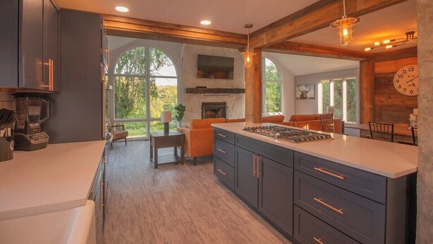 A modern kitchen with dark cabinetry, a large island, and a stone fireplace. -  7 bedrooms, 4 bathrooms, located in Beach Lake, PA. Sleeps 16, Max capacity  21 (Beach Lake)