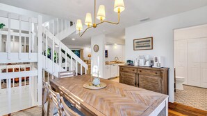 A modern interior with a wooden herringbone floor, a white staircase, a kitchen area with a coffee maker, and a framed quote on the wall. - 1 Block to Beach | Golf Cart + Heated Pool (Holmes Beach)