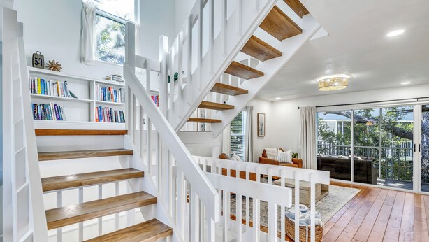 A modern staircase with wooden steps and white railings, leading to a living area with a sofa and a large window. - 1 Block to Beach | Golf Cart + Heated Pool (Holmes Beach)