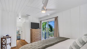 A bedroom with a bed, a TV, a dresser, and a view of palm trees through the window. - 1 Block to Beach | Golf Cart + Heated Pool (Holmes Beach)