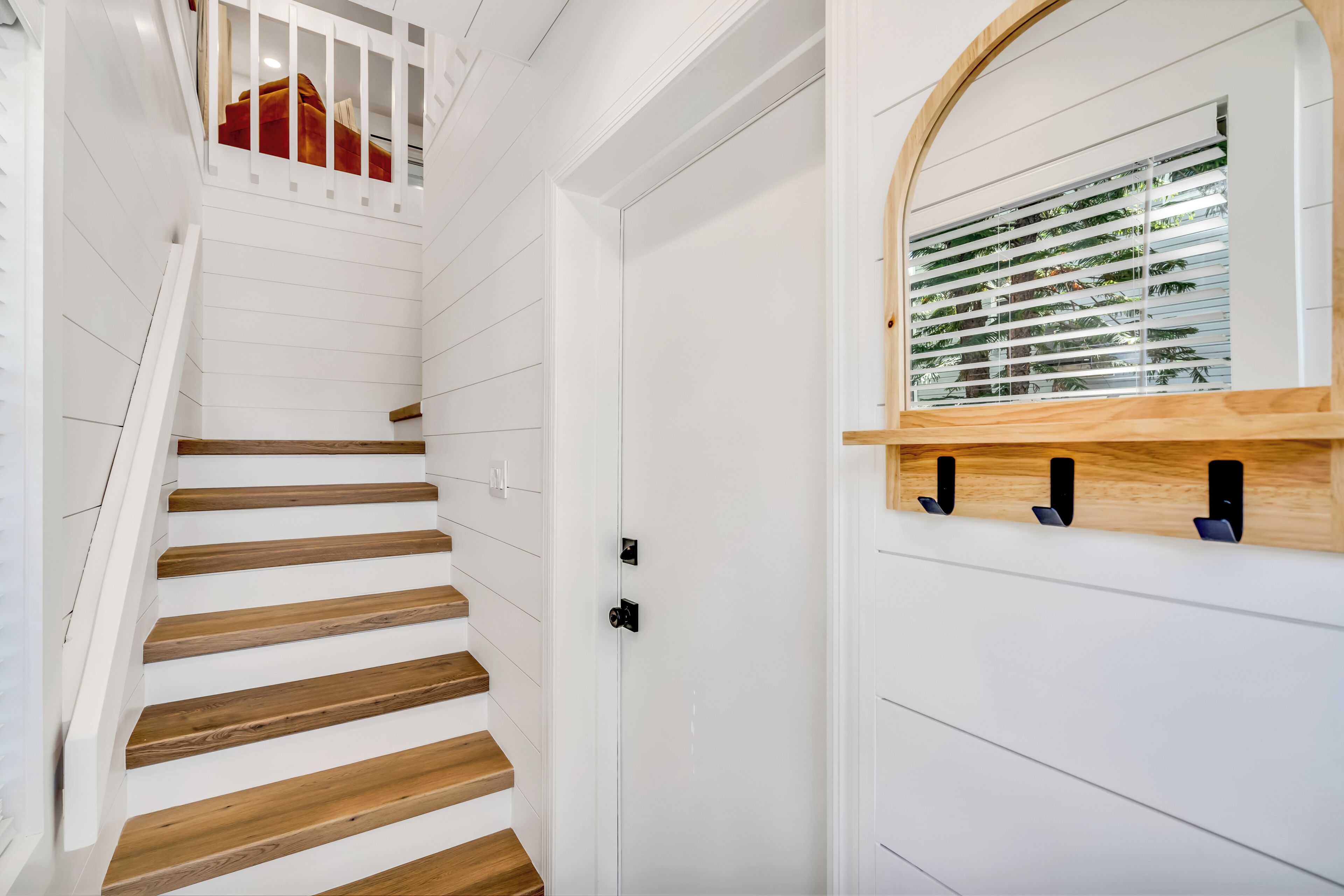 A staircase with wooden steps and white walls, leading to a door with a window above.