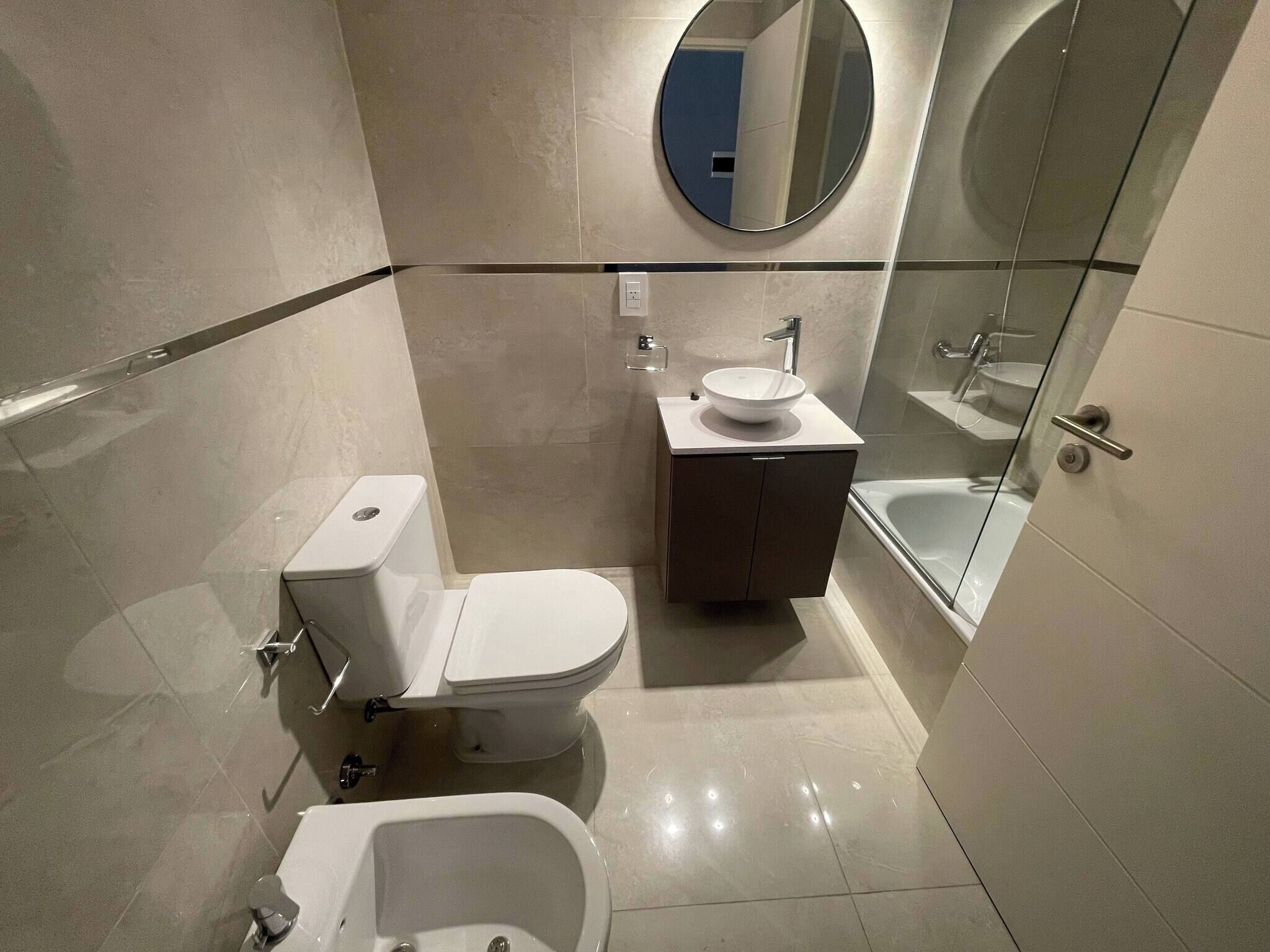 Et moderne badeværelse med toilet, bidet, vask og en bruseniche med glasvægge.
